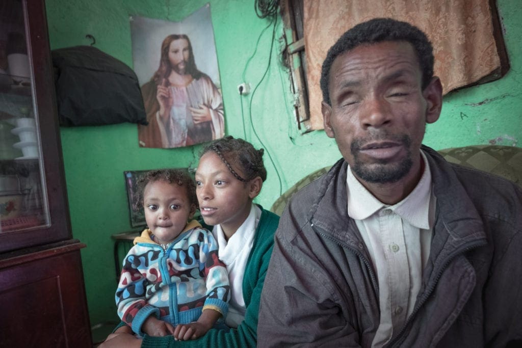 Blind father sits beside two daughters in their home.