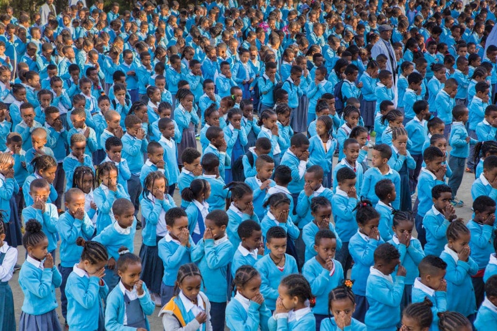 A great many students line up outside in matching blue uniforms.