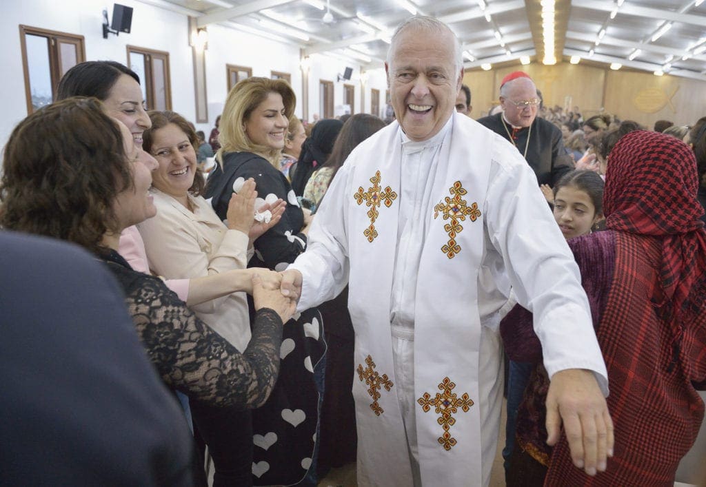 Msgr. Kozar shakes hands while greeting members of a crowd, with Cardinal Timothy Dolan doing likewise in the background.