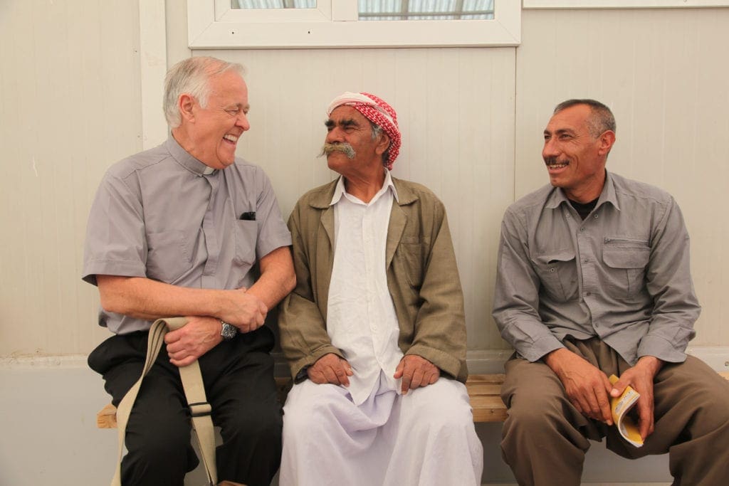 john kozar chats with two Iraqi men while seated on a bench beside them.