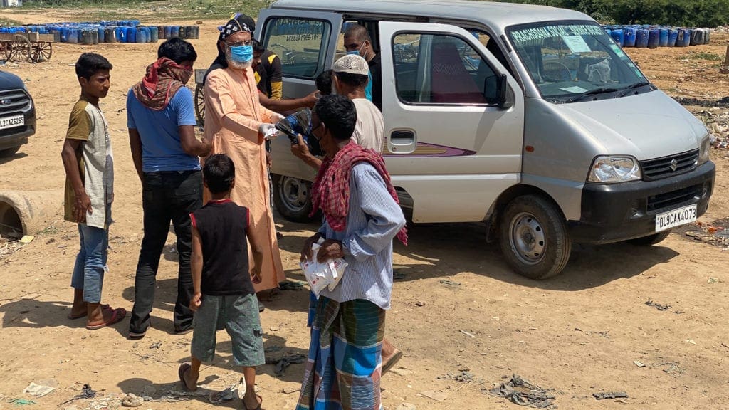 the archbishop, wearing a surgical mask and gloves, hands out supplies from a to people of all ages gathered outside a van.