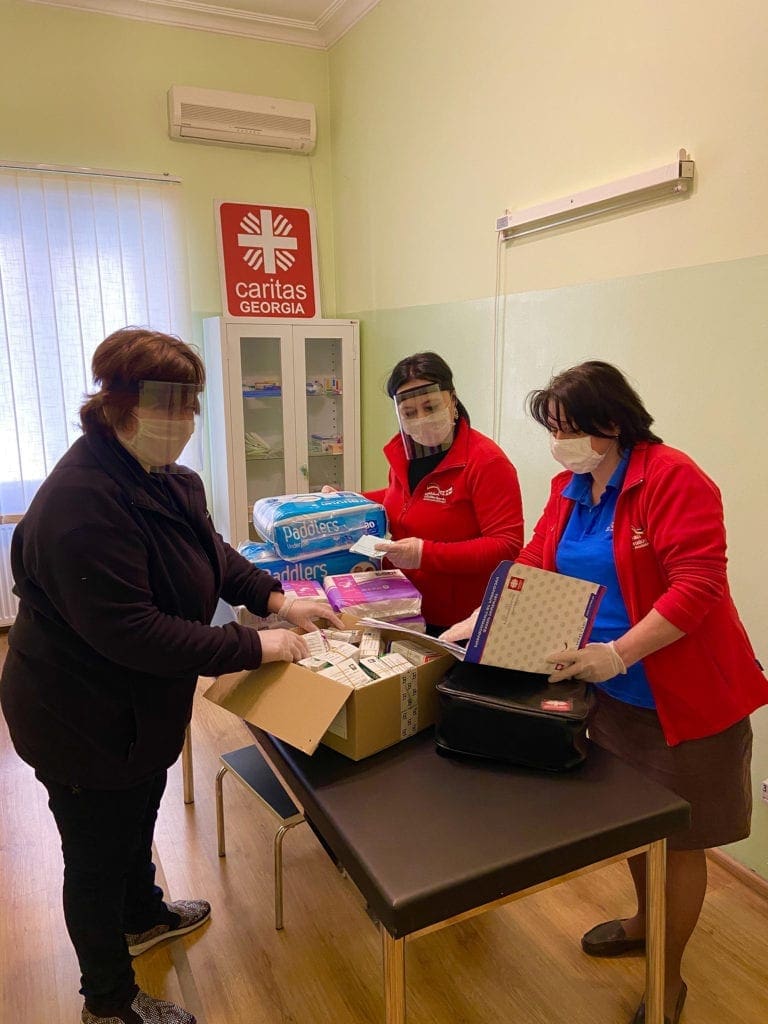 three women in protective masks sort boxes and review inventories at a table.