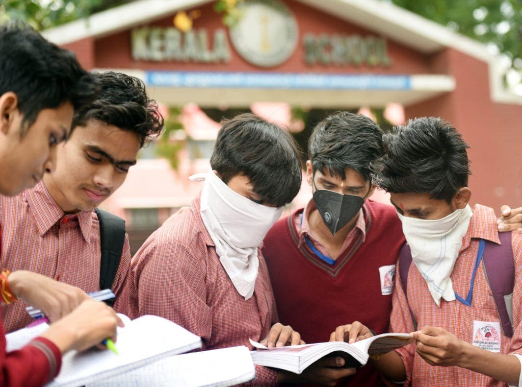 Five young men, several wearing masks, gather to pore over books.