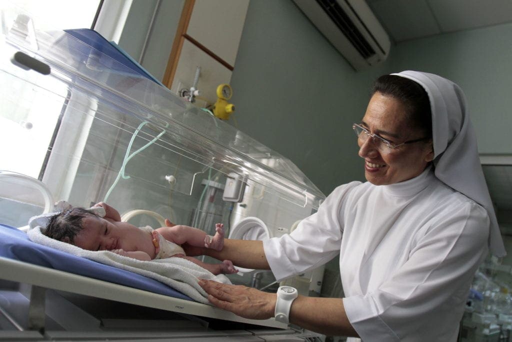 a nun performs a checkup on a small baby in an incubation unit.