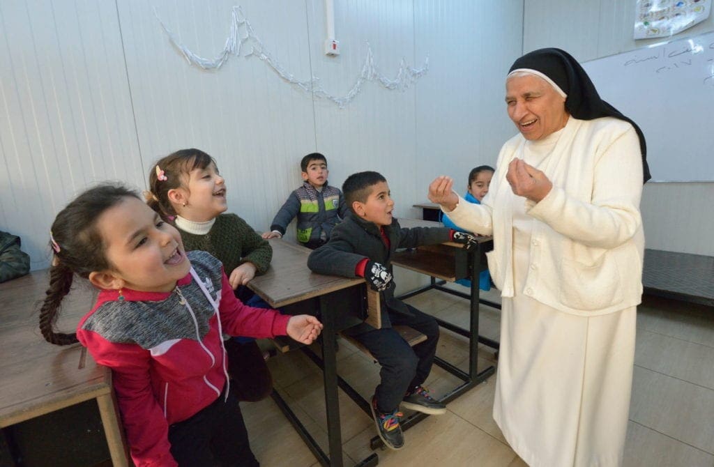 a nun laughs and gestures with both hands while lecturing a classroom of young students in the middle east.