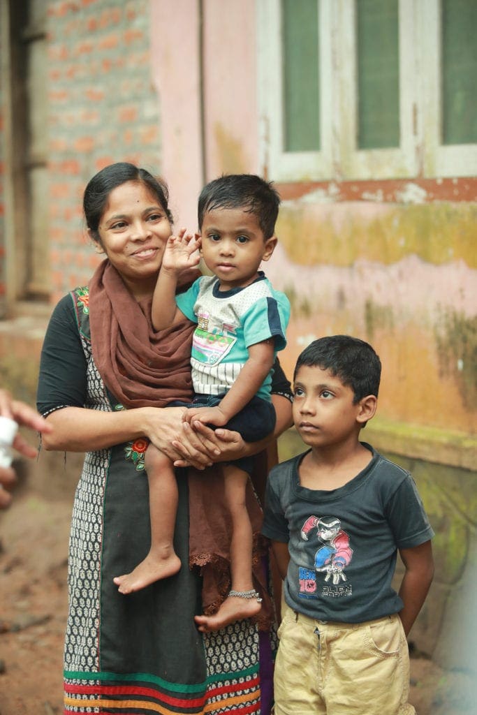 a young woman holds her younger son while her elder son stands beside her.