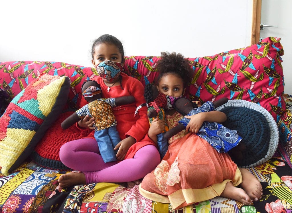 Two 5-year-olds hold dolls as they sit together on a comfy couch.