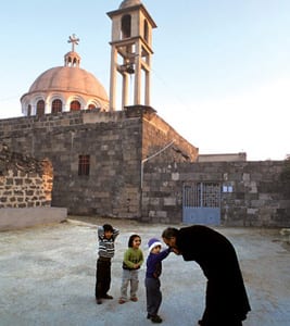 In 2004, Father Elias Hanout greeted children in front of St. Elias Melkite Greek Catholic Church in the southern Syrian town of Ezraa. The church, which dates to the sixth century and is among the oldest churches in the world, is in jeopardy as rebel forces close in on the largely Christian town. (photo: Armineh Johannes)