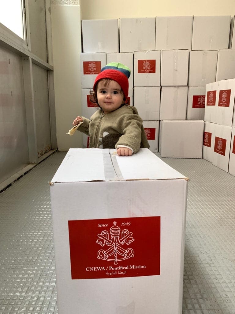 a young child stands near boxes of aid supplies.