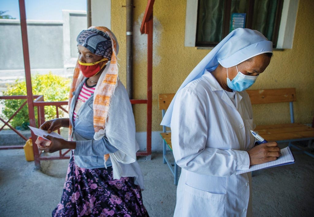 a masked nun writes on a pad of paper.