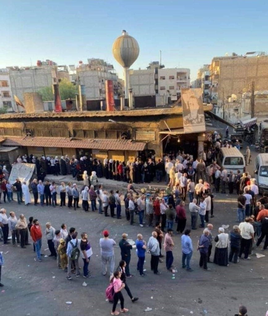 long line of people wait to buy bread in damascus