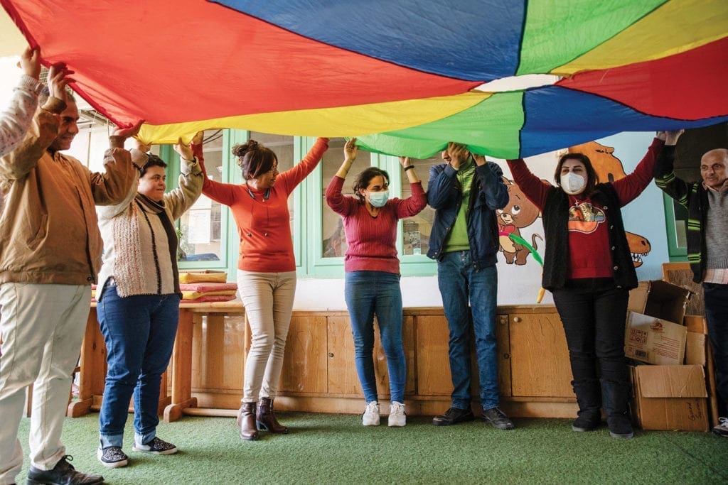 people standing in a circle raise a parachute in the air.