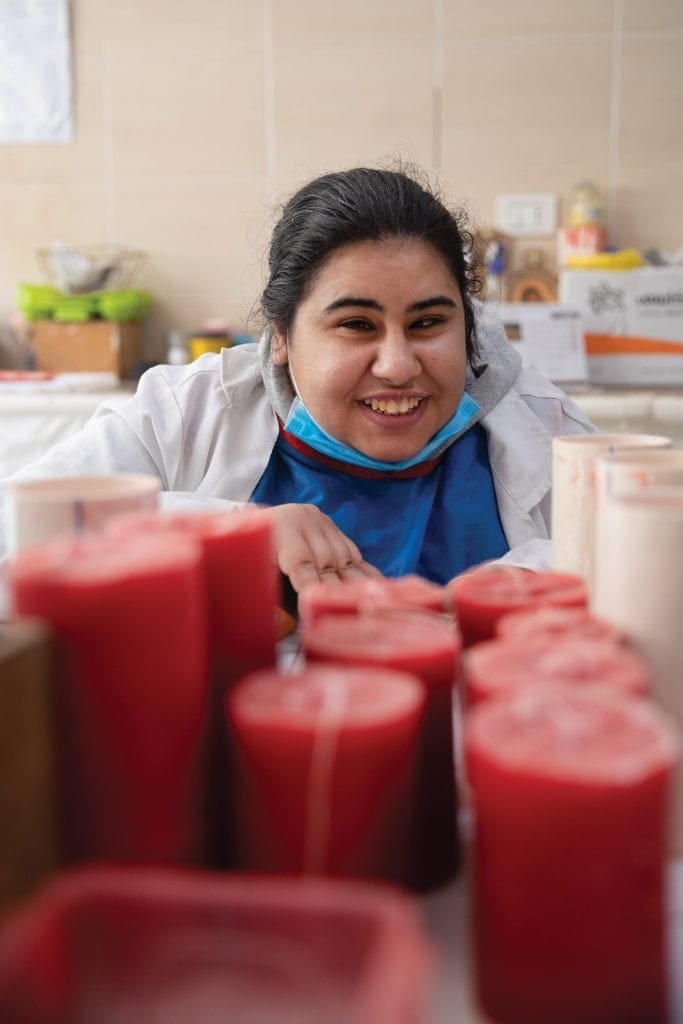 a young woman smiles from behind freshly made candles.