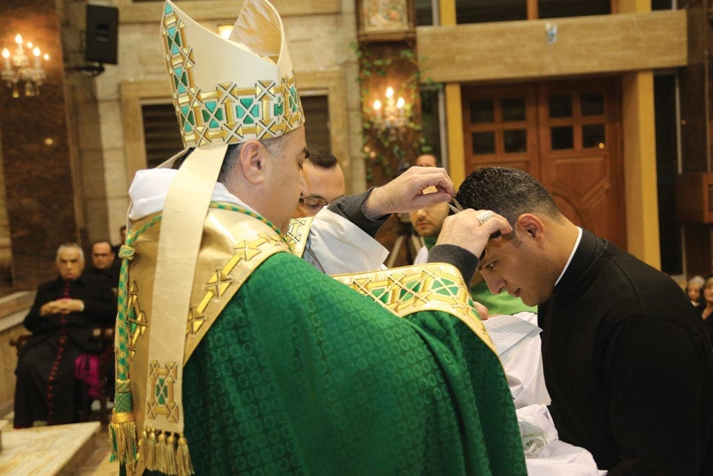 a bishop cuts a seminarian's hair with scissors.