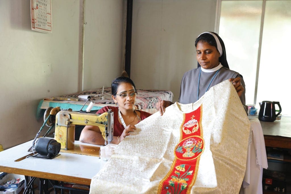 a nun inspects a vestment stitched by a woman seated adjacent.