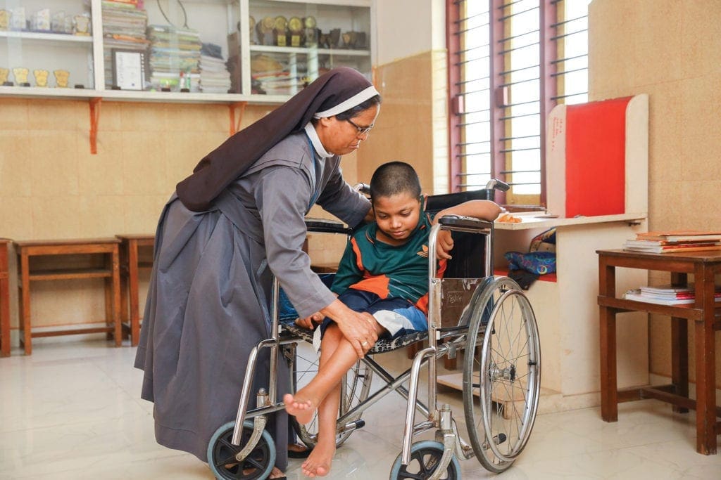 a nun assists a child in a wheelchair.