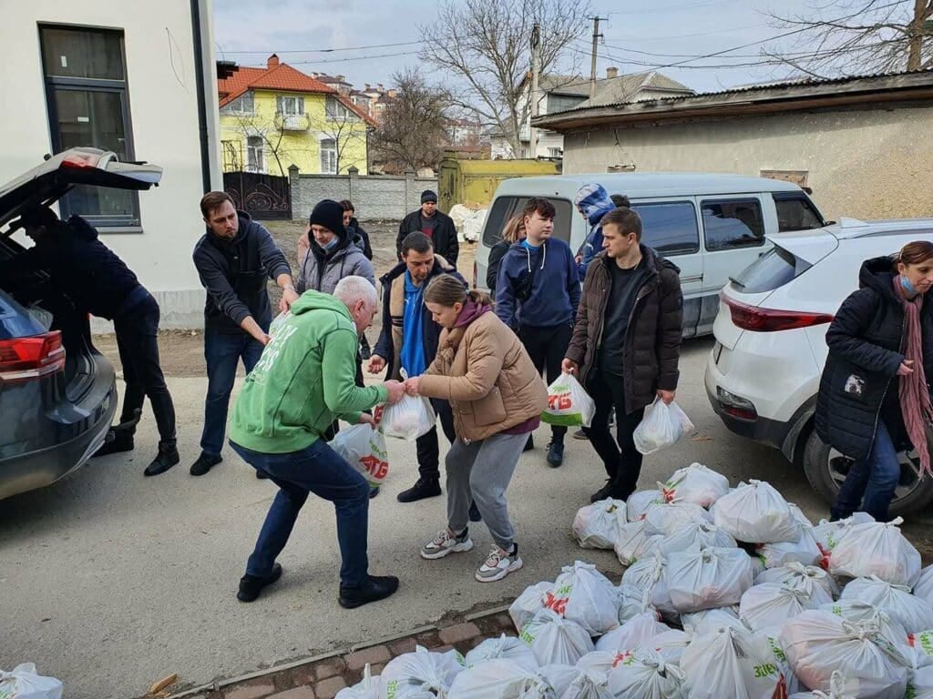 people hand out food packages outdoors in Ukraine.