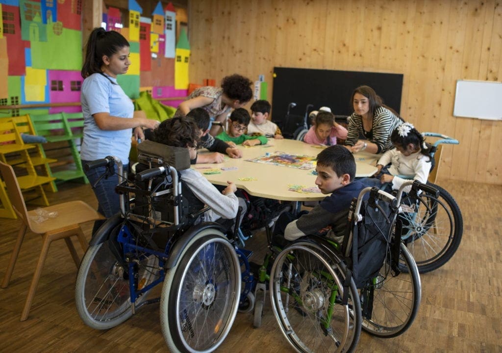 Armenian children, some in wheel chairs, sit around a large table playing a board game.