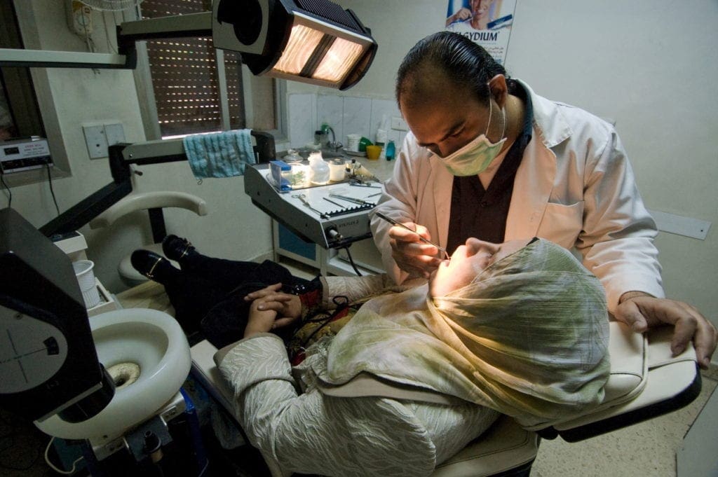 a dentist gives a woman in a headscarf a checkup in Aleppo.