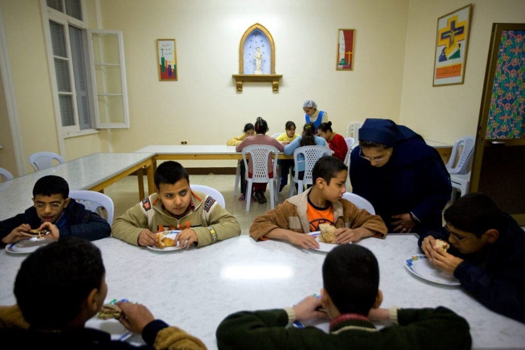 a nun talks to a children seated at a lunch table in Alexandria.