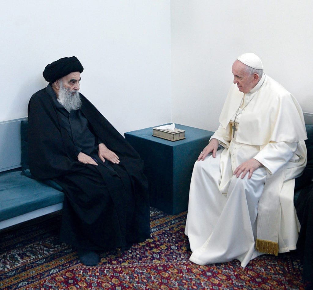 Pope Francis and Grand Ayatollah Ali al Sistani talk, both seated.