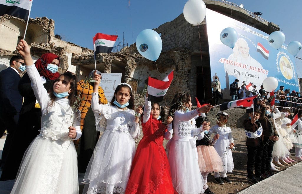 children hold balloons and wave tiny flags by the side of the street.