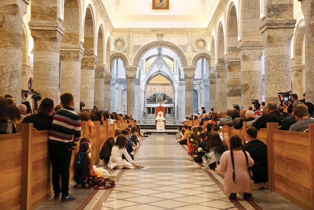 the pope sits at the nave of a large, crowded church in Iraq.