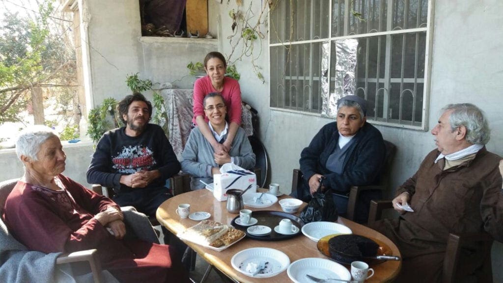 sister jihane atallah sits with a family around a table outdoors, drinking coffee.