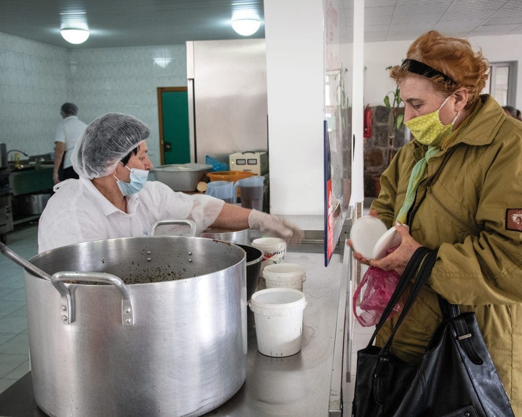 a woman in a mask collects food at the soup kitchen in Kutaisi, Georgia.