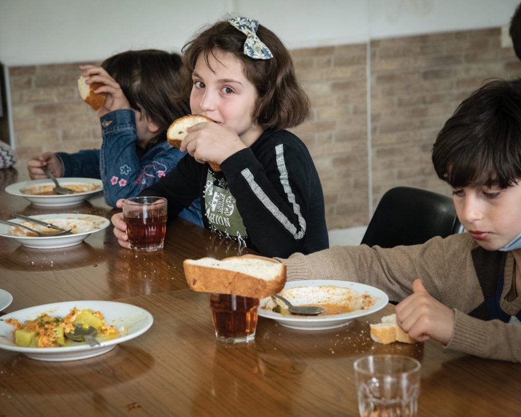 a girl eats bread with her soup at a large table.