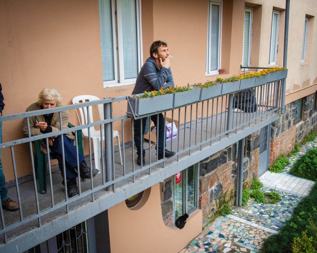 a georgian man leans against a balcony railing, smoking a cigarette.