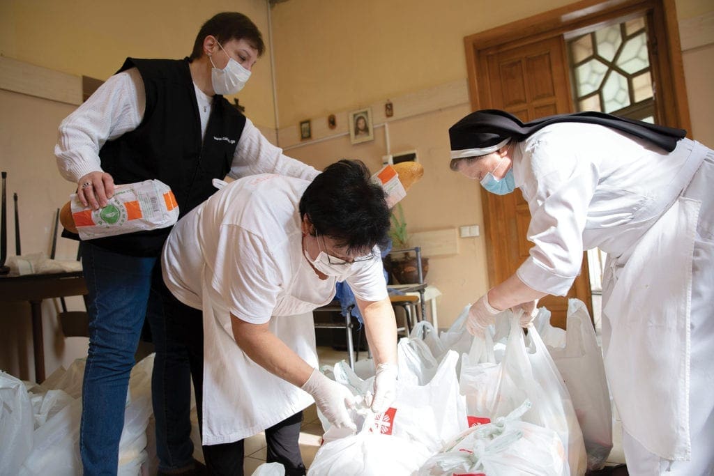 a nun and two caritas staff members tie up bags of food.