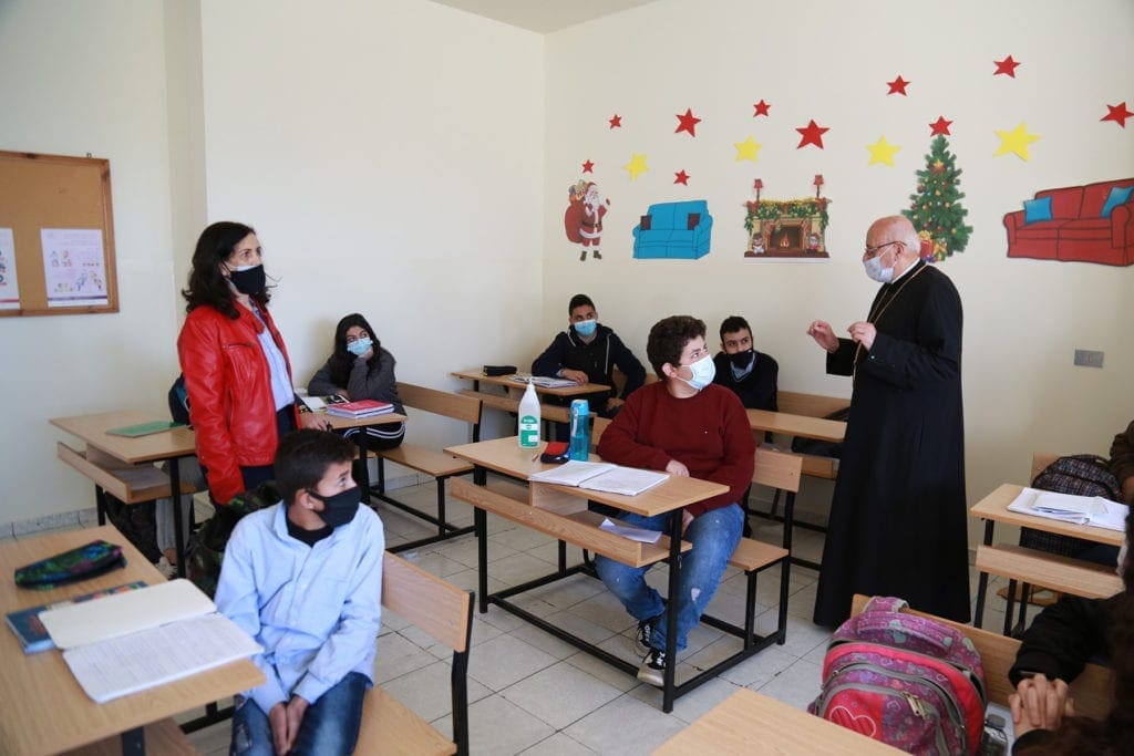 an archbishop in a mask addresses seated students..