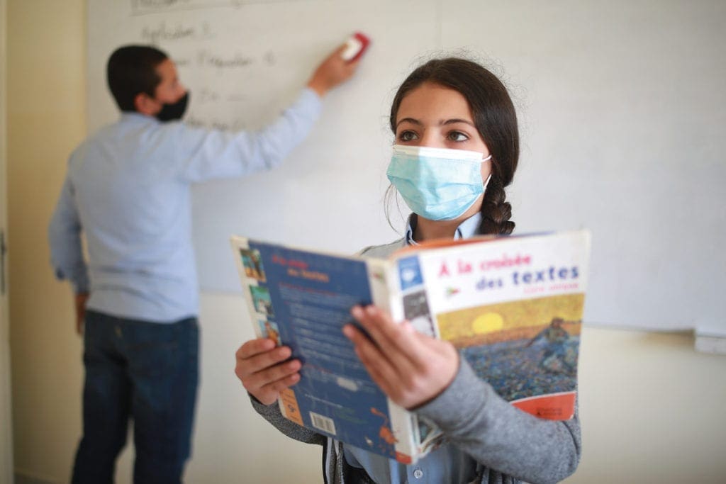 an adolescent girl stands with a text book in class.