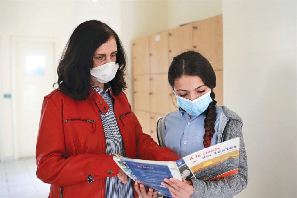 a woman and a girl look at a textbook together.