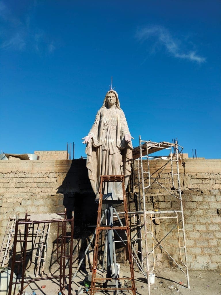 a statue of Mary being raised up over a wall.