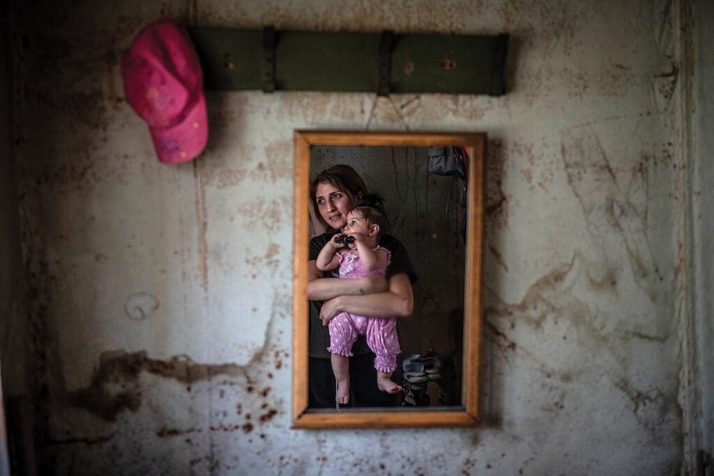 a mother and child are reflected in a small mirror on a weathered wall of a domik.