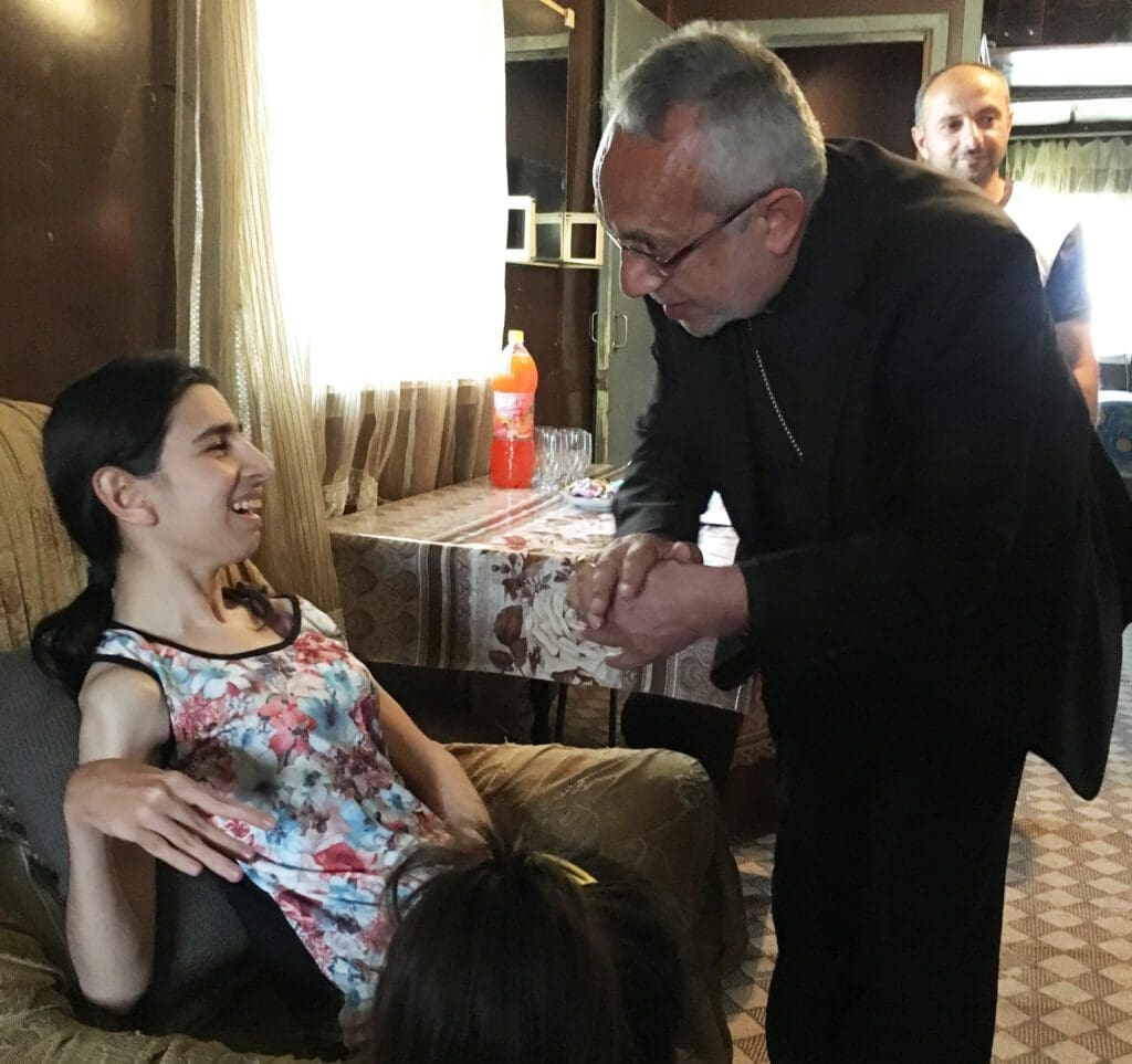 Archbishop Raphael Minassian visits with a young woman with disabilities during a pastoral visit to families along the Turkish border in 2017.