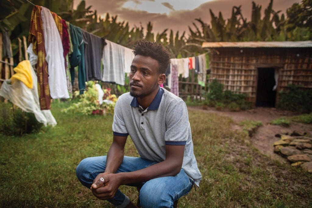 university student in ethiopia sits outside with laundry drying on a line behind him.