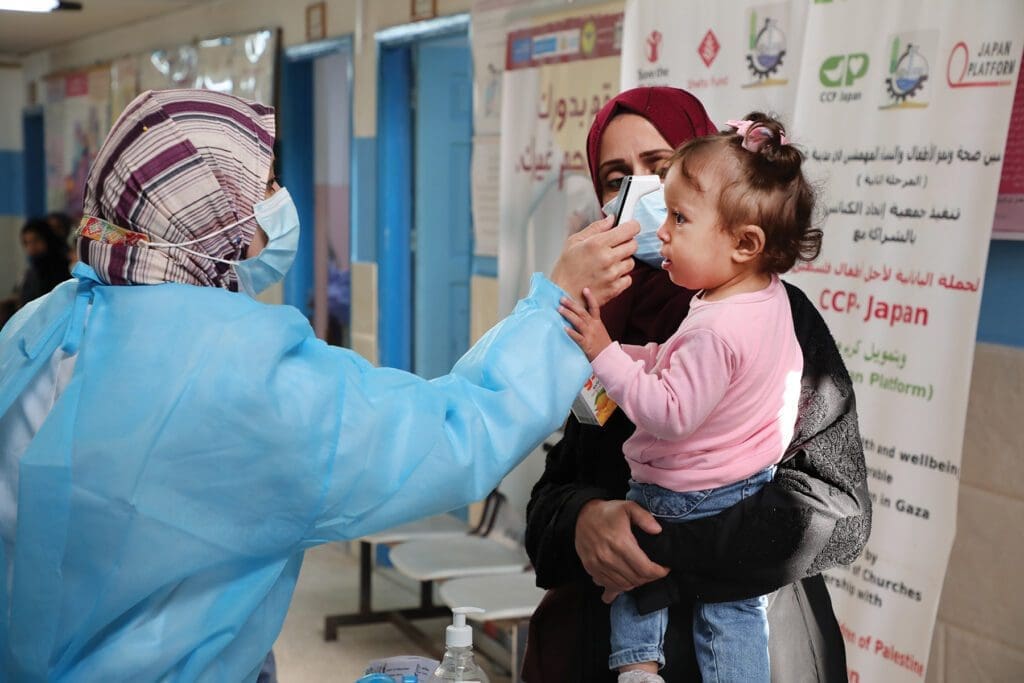 a young girl held by her mother, receives a checkup from a medical staffer in a smock.