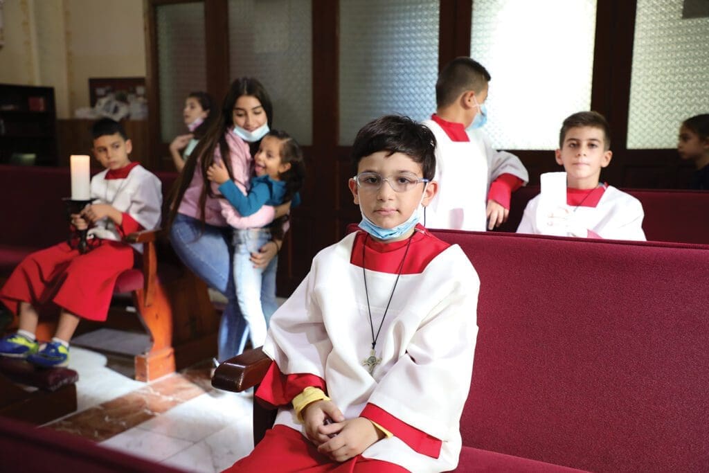 children in altar server robes sit on benches.