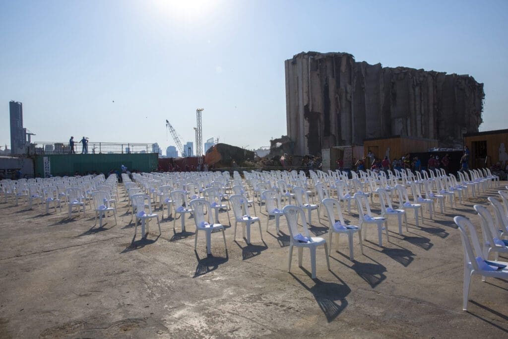 Empty white chairs placed for an open Mass in front smoldering debris in Beirut