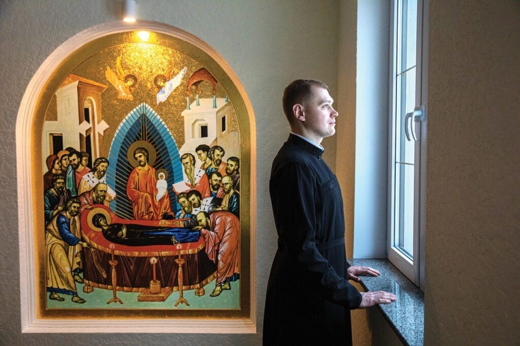 A seminarian looks out the window, an icon is to his left