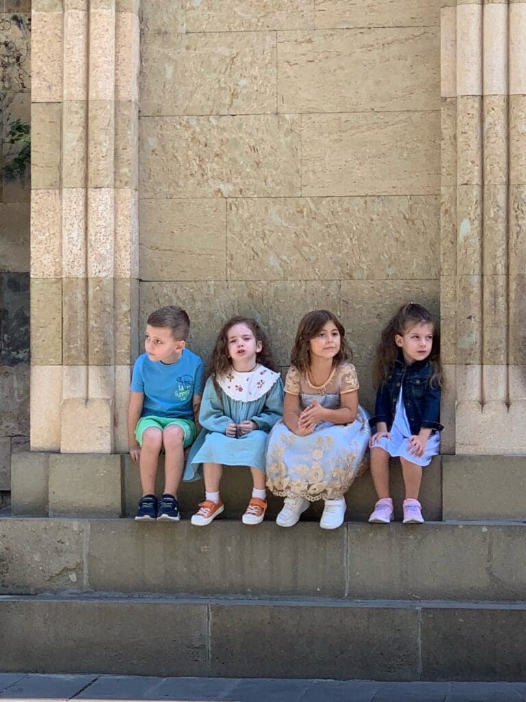 Four children sit in a row outside of a church