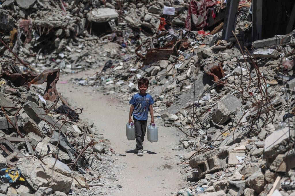 A displaced boy fetches water in a camp in northern Gaza amid the rubble.