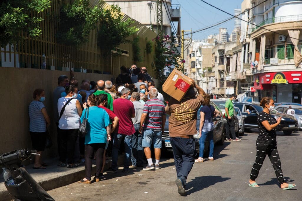 A crowded street. One man walks with a carton box on his shoulder.