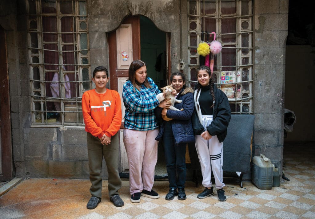 A woman and there young children standing in from of a house. One of the children is holding a cat.