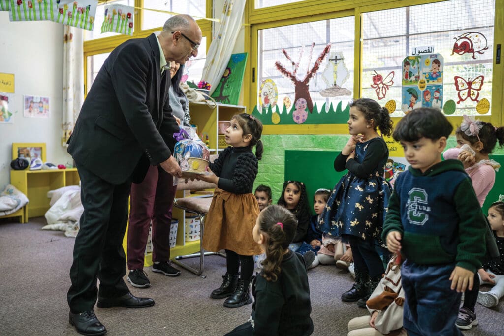 A man wearing a suit greets children at a school.