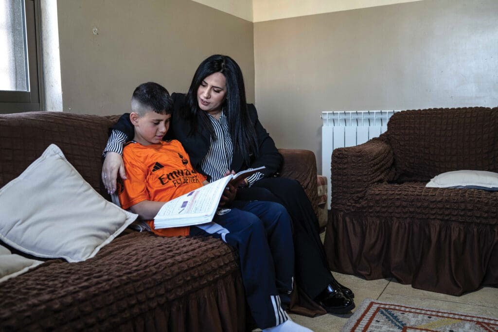 A woman embraces a boy who is reading a book. They are sitting on a couch.
