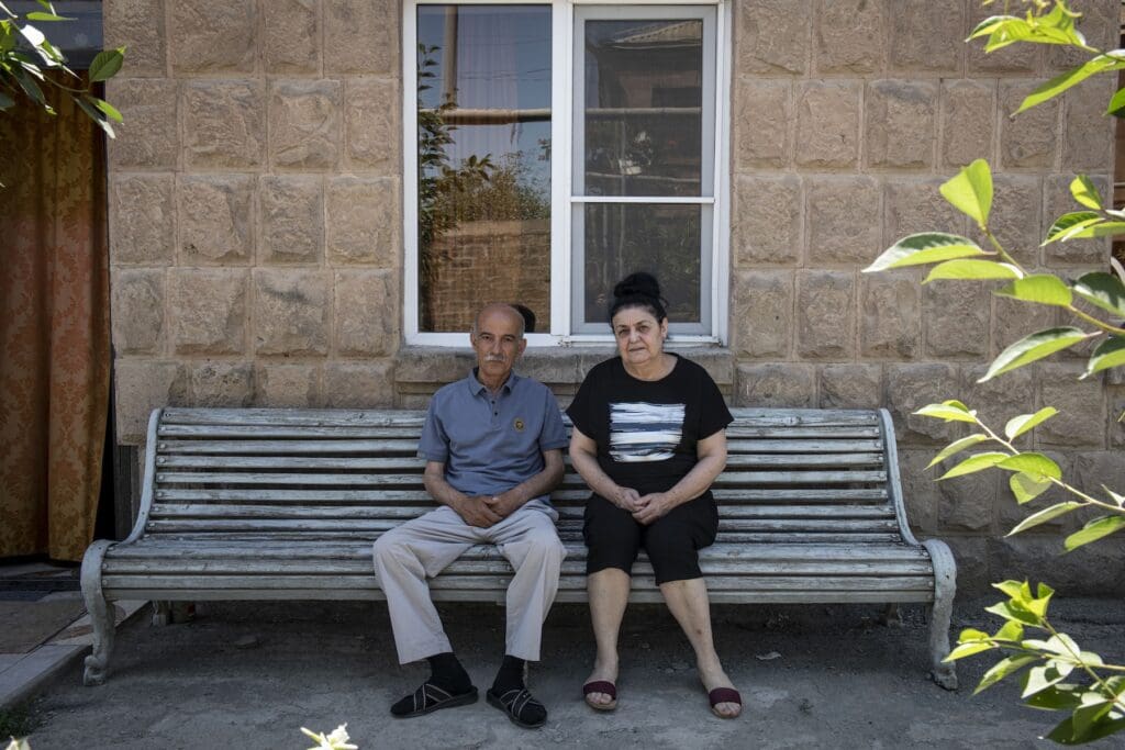 A couple of elderly people, man and woman, sitting at a bench.